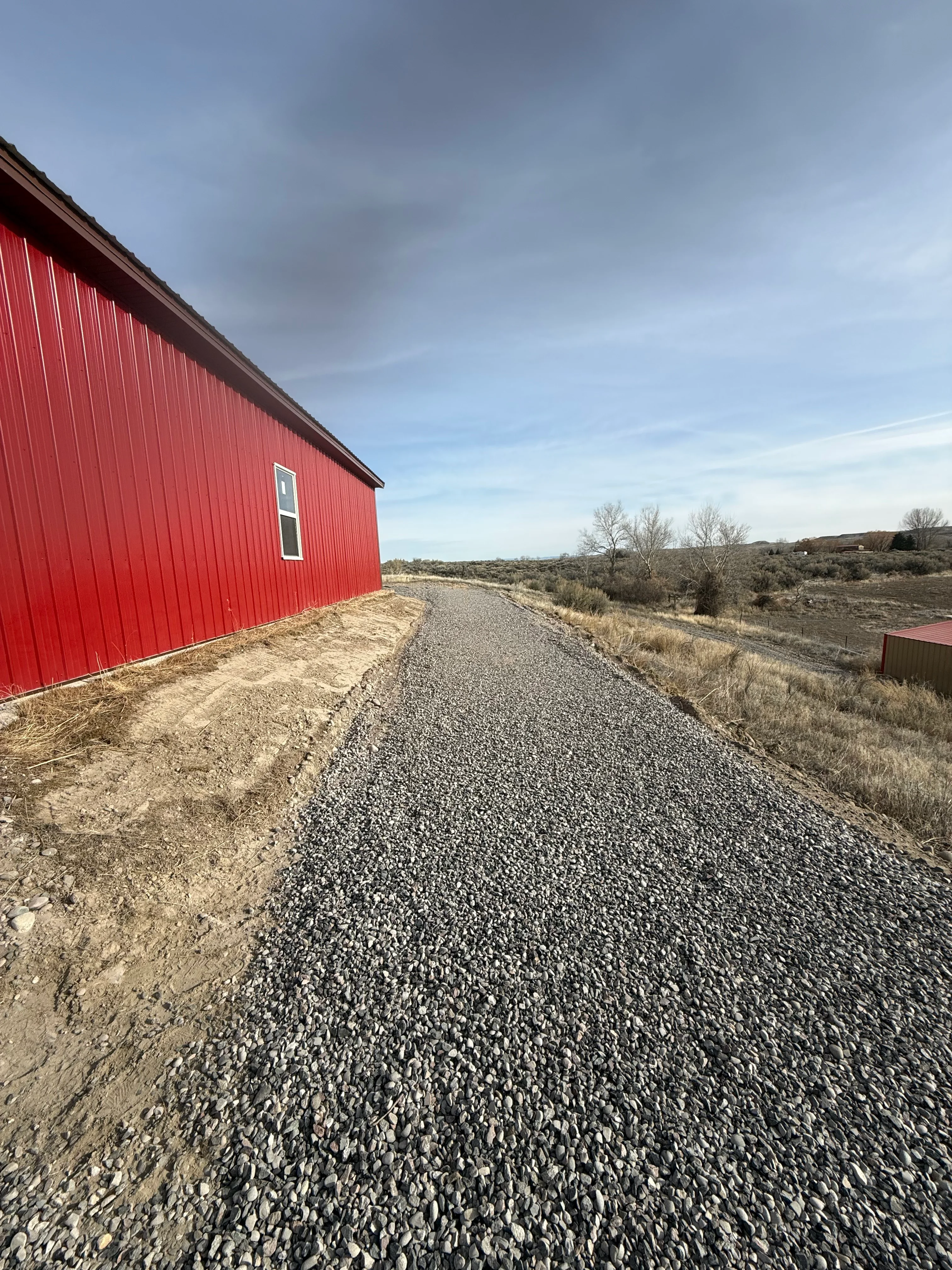 Gravel driveway with crushed stone base next to red metal building structure