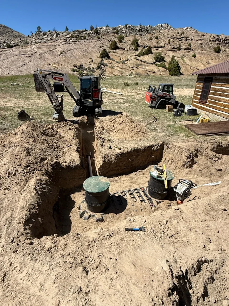 Mini excavator installing septic tanks and drain field with equipment on site