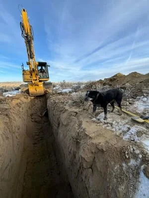 Yellow tracked excavator digging deep trench in rocky soil with bucket extended