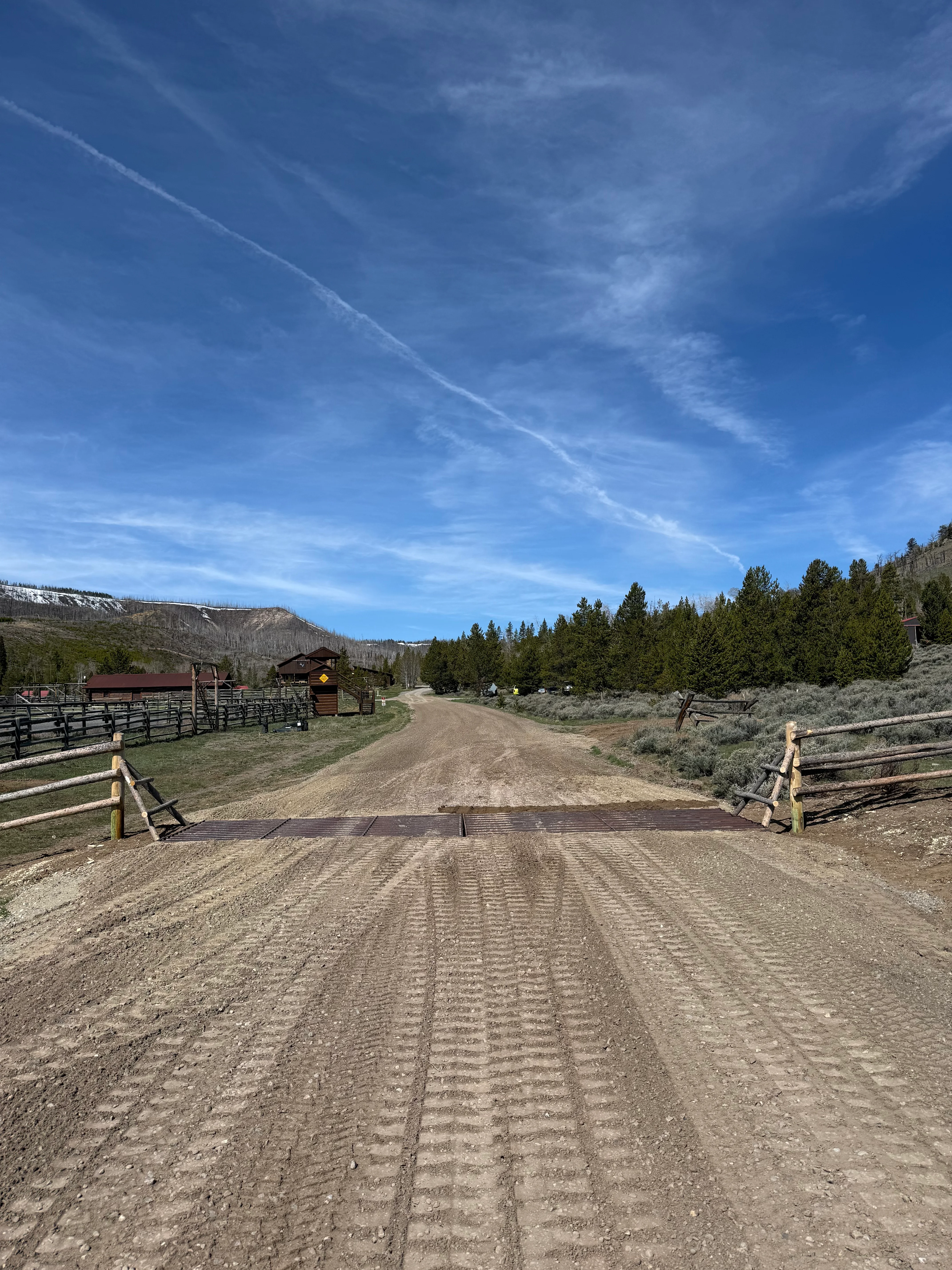 Graded dirt driveway with cattle guard, split-rail fencing, and compacted base material on ranch property