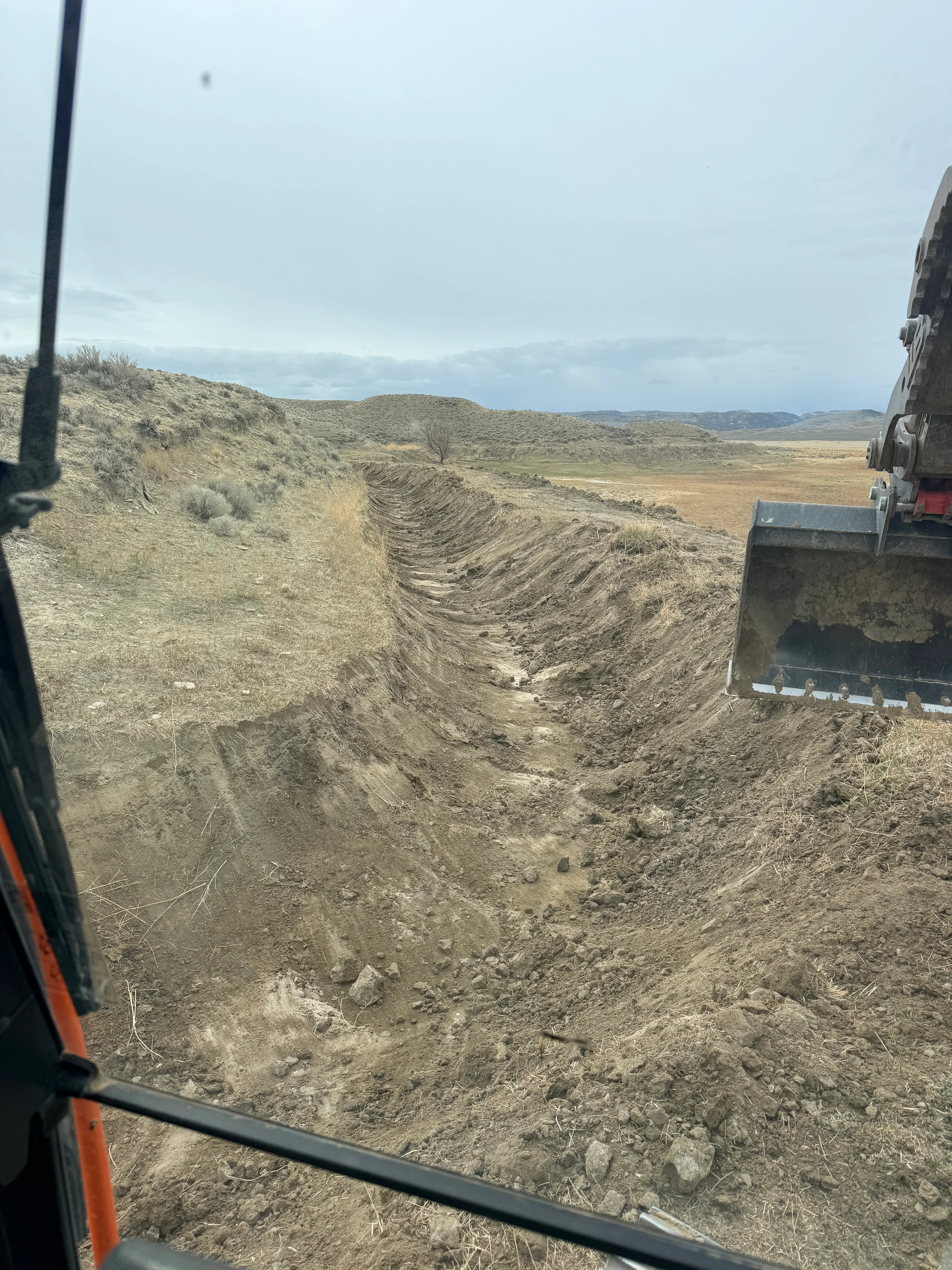 Deep excavated trench with graded slopes and heavy equipment on rural terrain