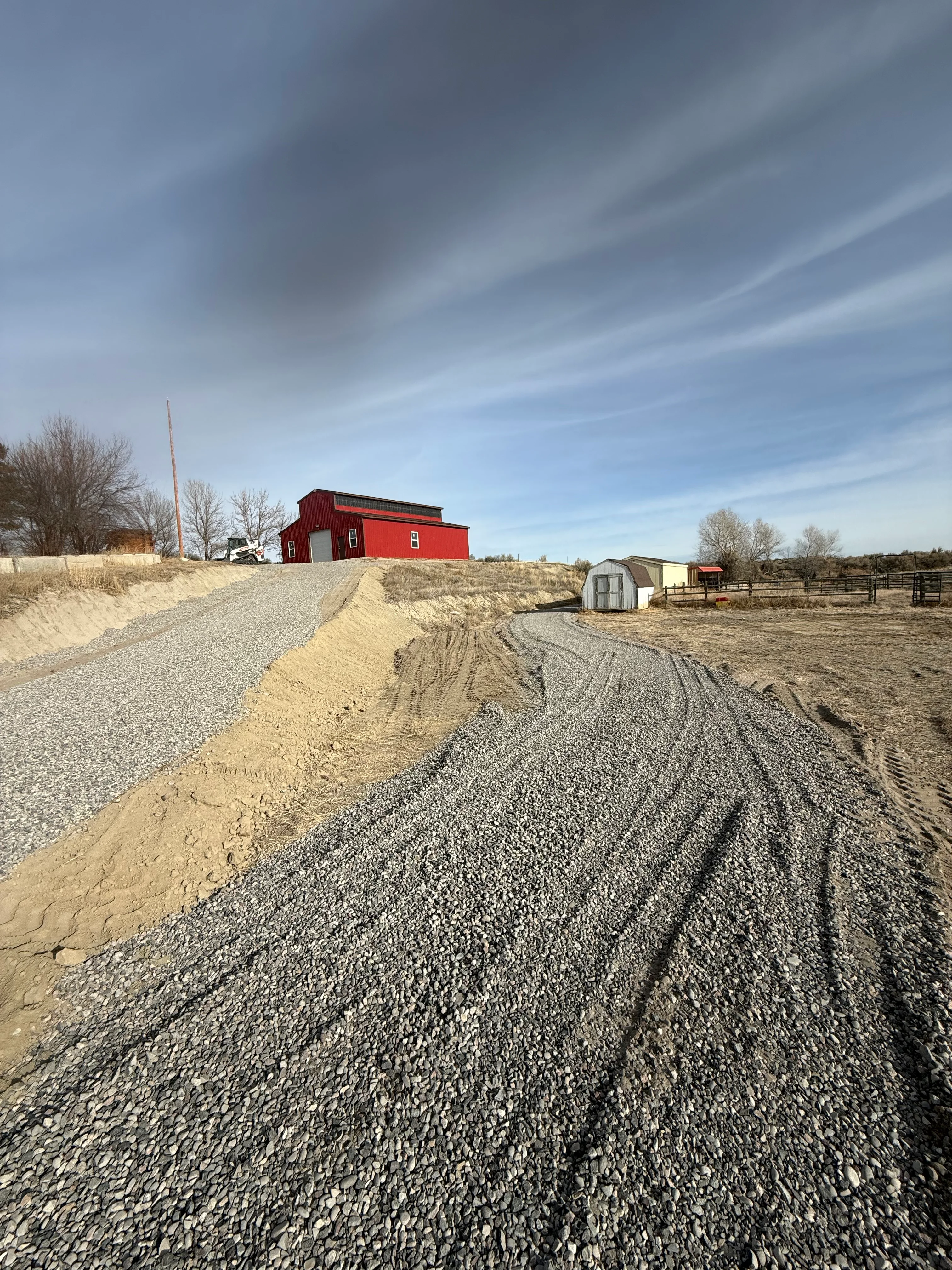 Gravel driveway with crushed stone base and graded earth shoulders on rural property