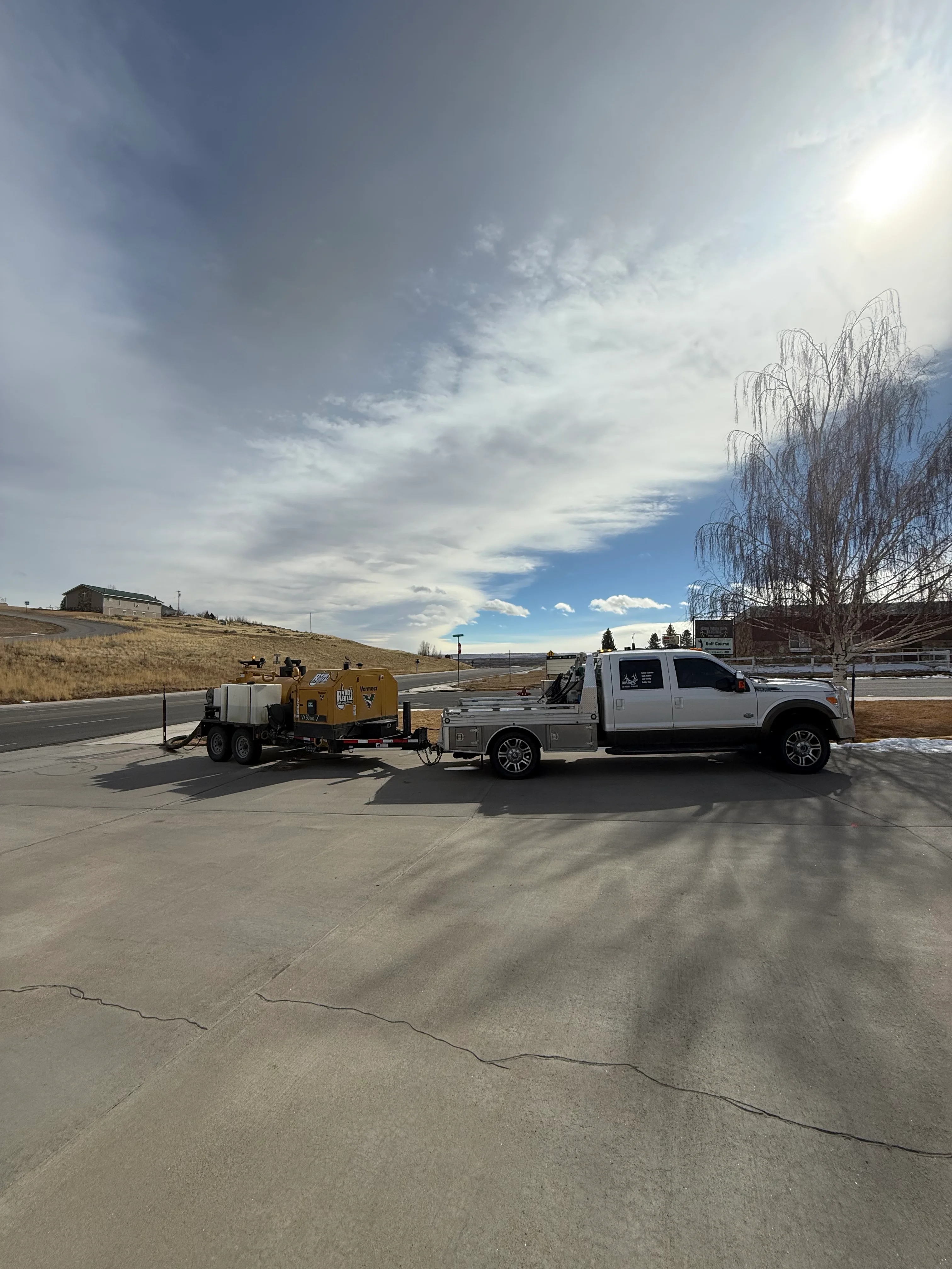 Yellow CAT excavator and white pickup truck on prepared concrete driveway with control joints