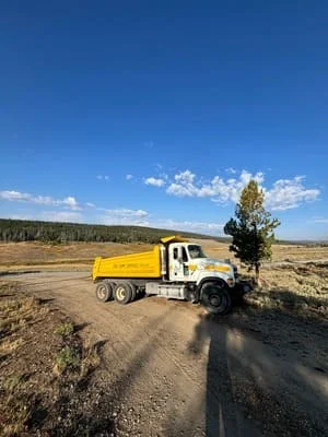 Yellow dump truck with gravel load on dirt road at cleared site