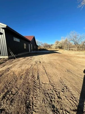 Graded dirt driveway with compacted base material in front of black metal residential building