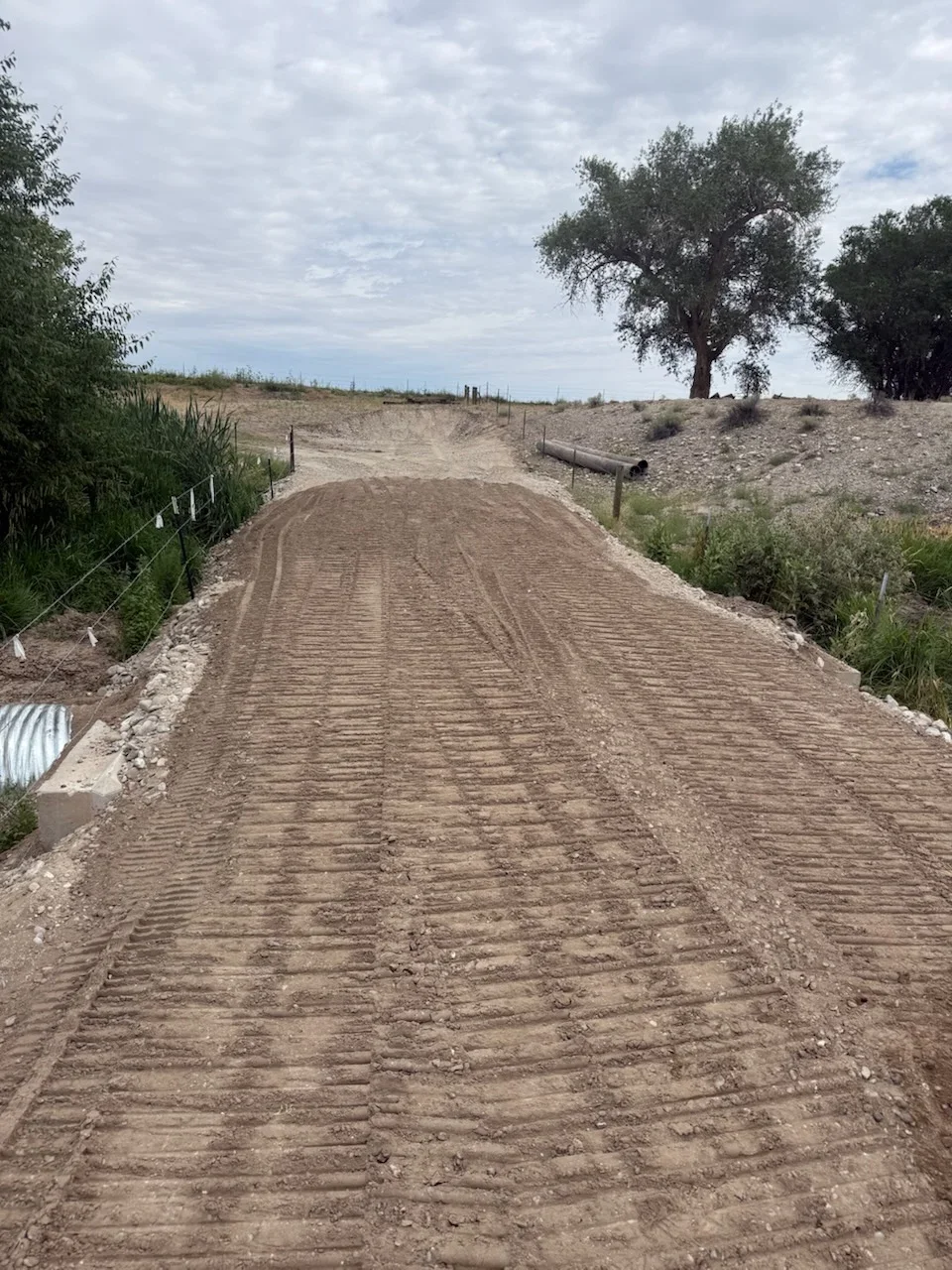 Freshly graded gravel driveway with compacted base and erosion control fencing on rural property
